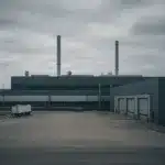 Vista ampla de uma planta automotiva em Camaçari, com galpões industriais e pátio logístico, em composição editorial sobre indústria e governança no Brasil.